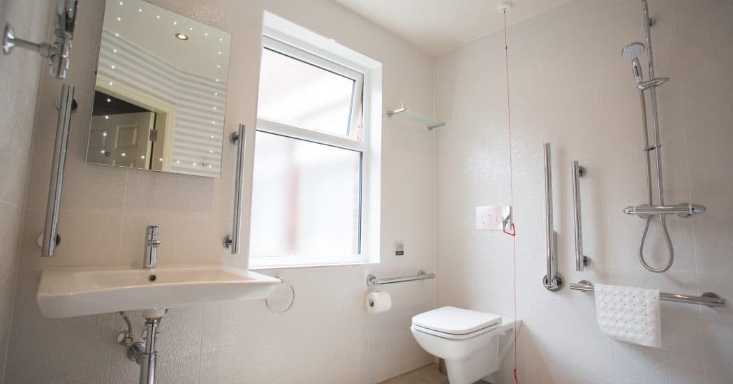 A simple hotel bathroom interior with white walls with toilet, shower, sink, window and mirror