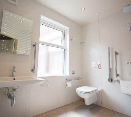 A simple hotel bathroom interior with white walls with toilet, shower, sink, window and mirror
