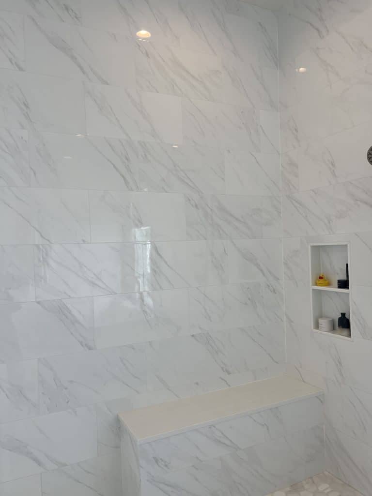 Walk-in shower with a built-in bench seat and marble tile walls in a New Orleans bathroom