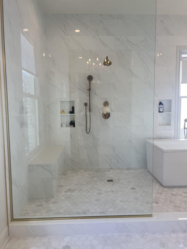 Glass-enclosed walk-in shower with marble tile, bench seat and gold fixtures