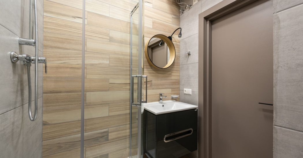 Compact modern bathroom with a glass walk-in shower, warm wood-look tile, and a floating vanity in a New Orleans home
