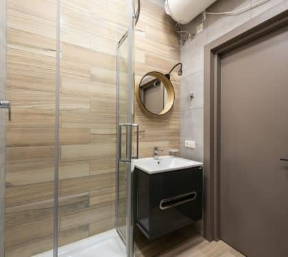 Compact modern bathroom with a glass walk-in shower, warm wood-look tile, and a floating vanity in a New Orleans home